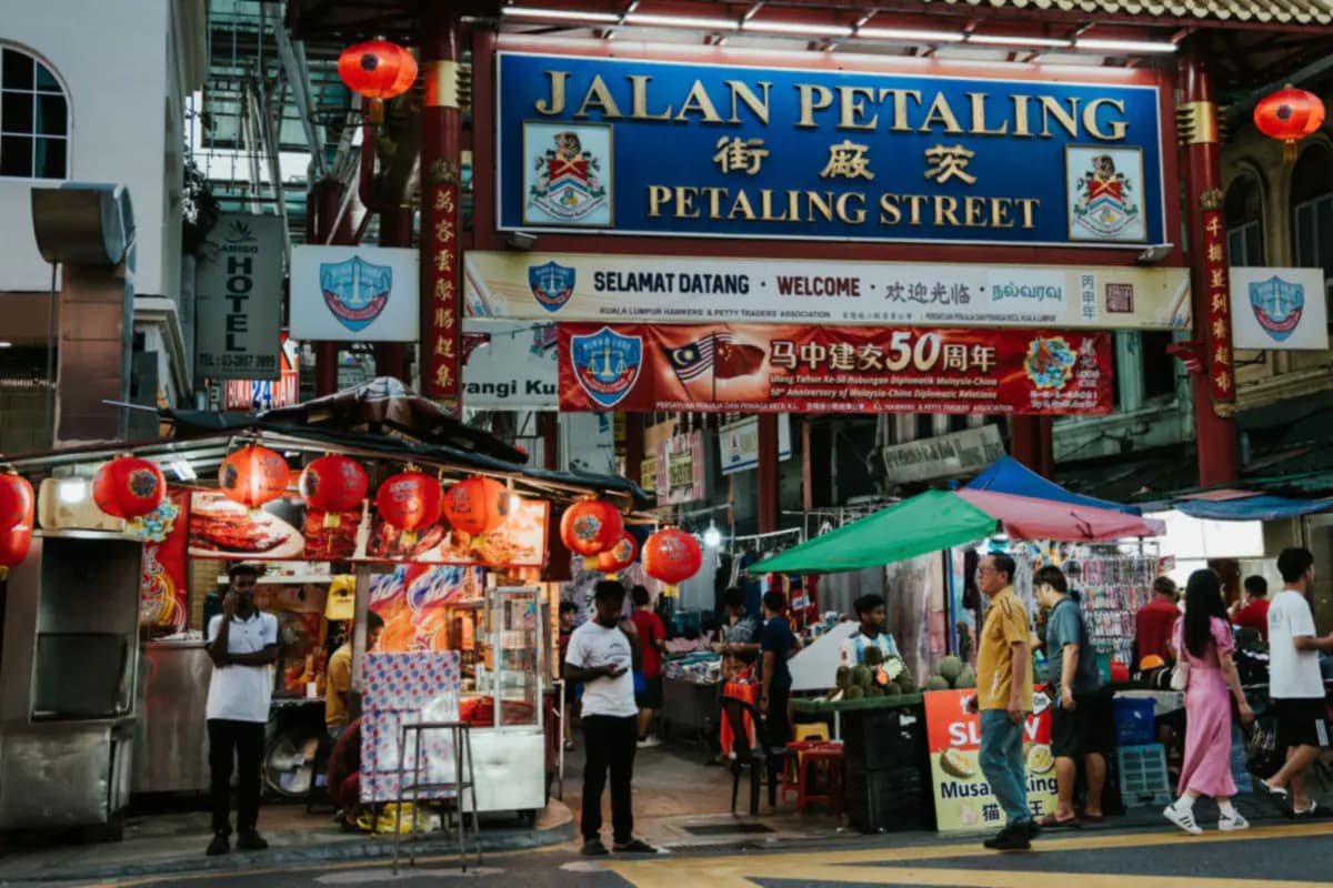 The gateway sign of Petaling Street in Kuala Lumpur above stalls hung with red lanterns, with people walking past