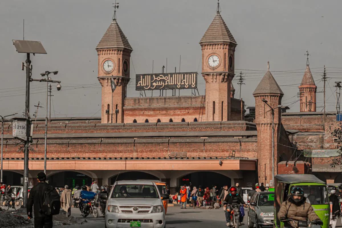 Brick clock towers above the entrance of the railway station in Lahore, with cars, motorbikes and rickshaws in the street