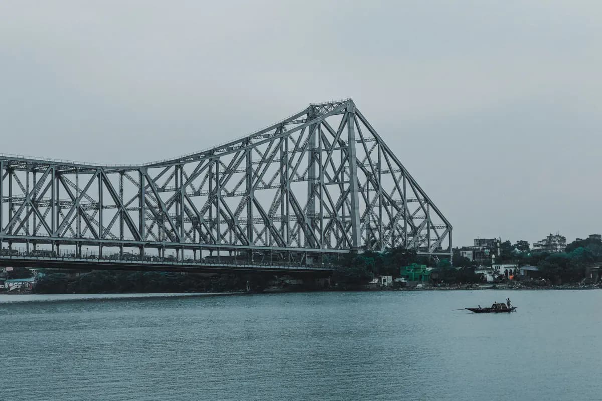 The steel lattice of Howrah Bridge over the Hooghly River in Kolkata, with a small wooden boat on the water below