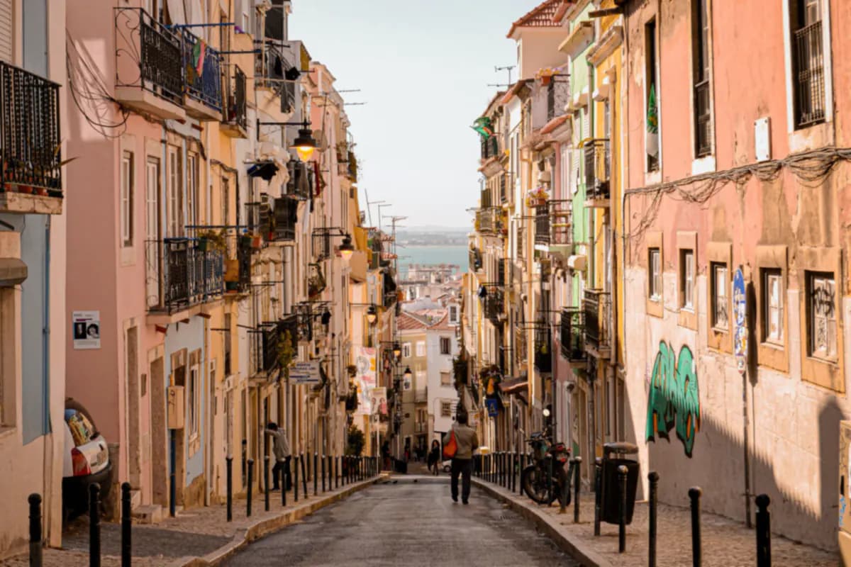A steep street in Lisbon lined with pastel houses and iron balconies, sloping down towards the river