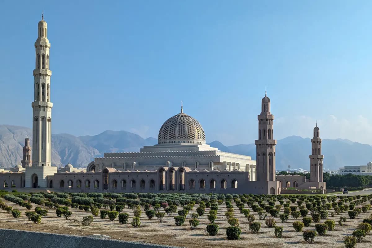 The Sultan Qaboos Grand Mosque in Muscat with its patterned dome and minarets, mountains behind and rows of shrubs in front
