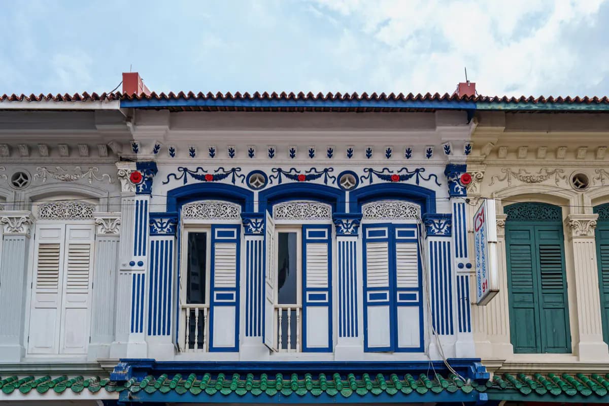 The upper floor of a blue and white shophouse in Little India, Singapore, with shuttered windows and ornate plasterwork