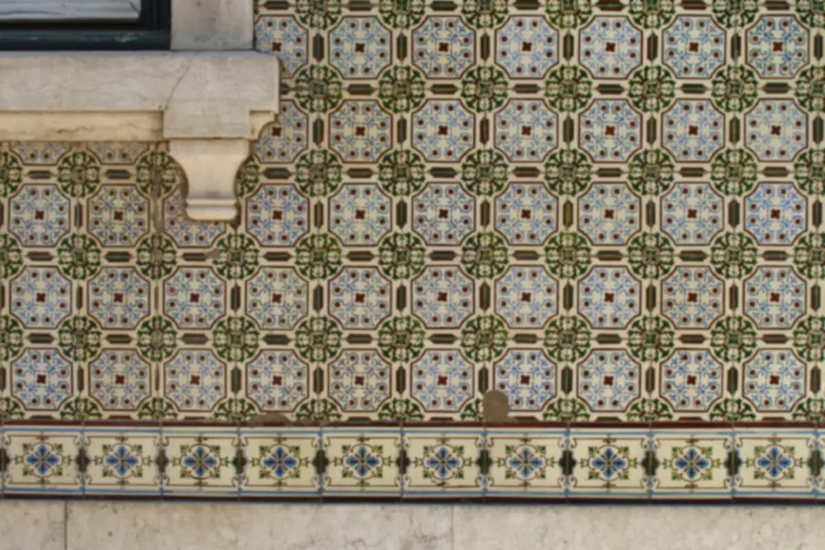 A wall of patterned blue, green and cream glazed tiles below a stone window ledge on a building in Lisbon