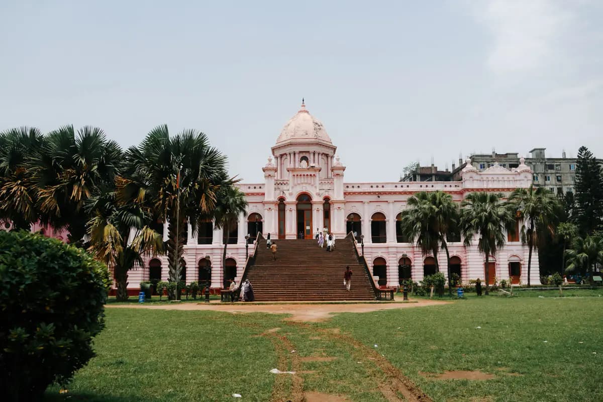 The pink domed Ahsan Manzil palace in Dhaka, with a wide staircase, palm trees and a lawn in front